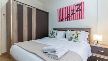 A hotel room with a bed, a nightstand, a lamp, a wardrobe, and a wall with a red and white striped artwork.