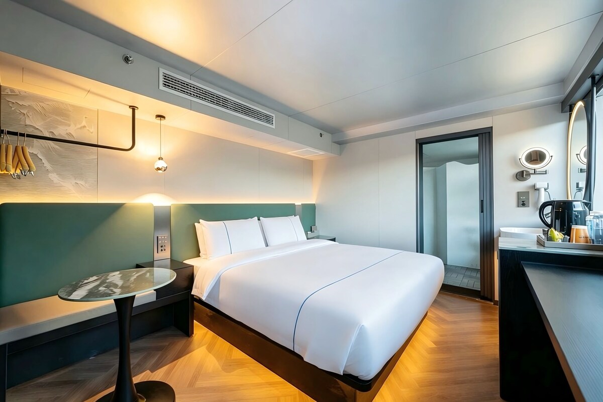 Una habitación de hotel con cama, mesita de noche, lámpara y vistas al baño.