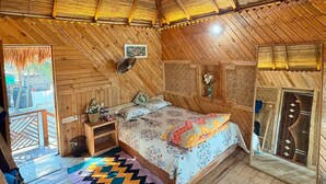 Un interior de madera con una cama, un ventilador y una alfombra colorida.