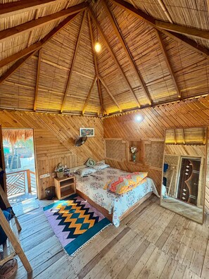Een houten interieur met een bed, een ventilator en een kleurrijk vloerkleed.
