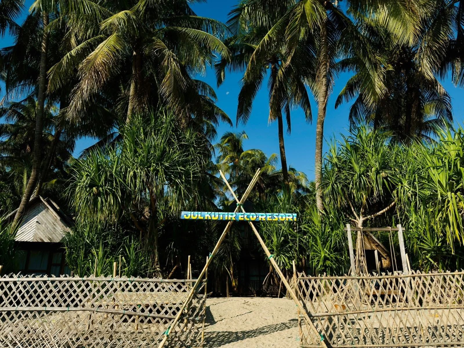 Une enseigne pour le complexe hôtelier écologique JUKUTIR ECO RESORT, avec une clôture en bambou et des palmiers en arrière-plan.