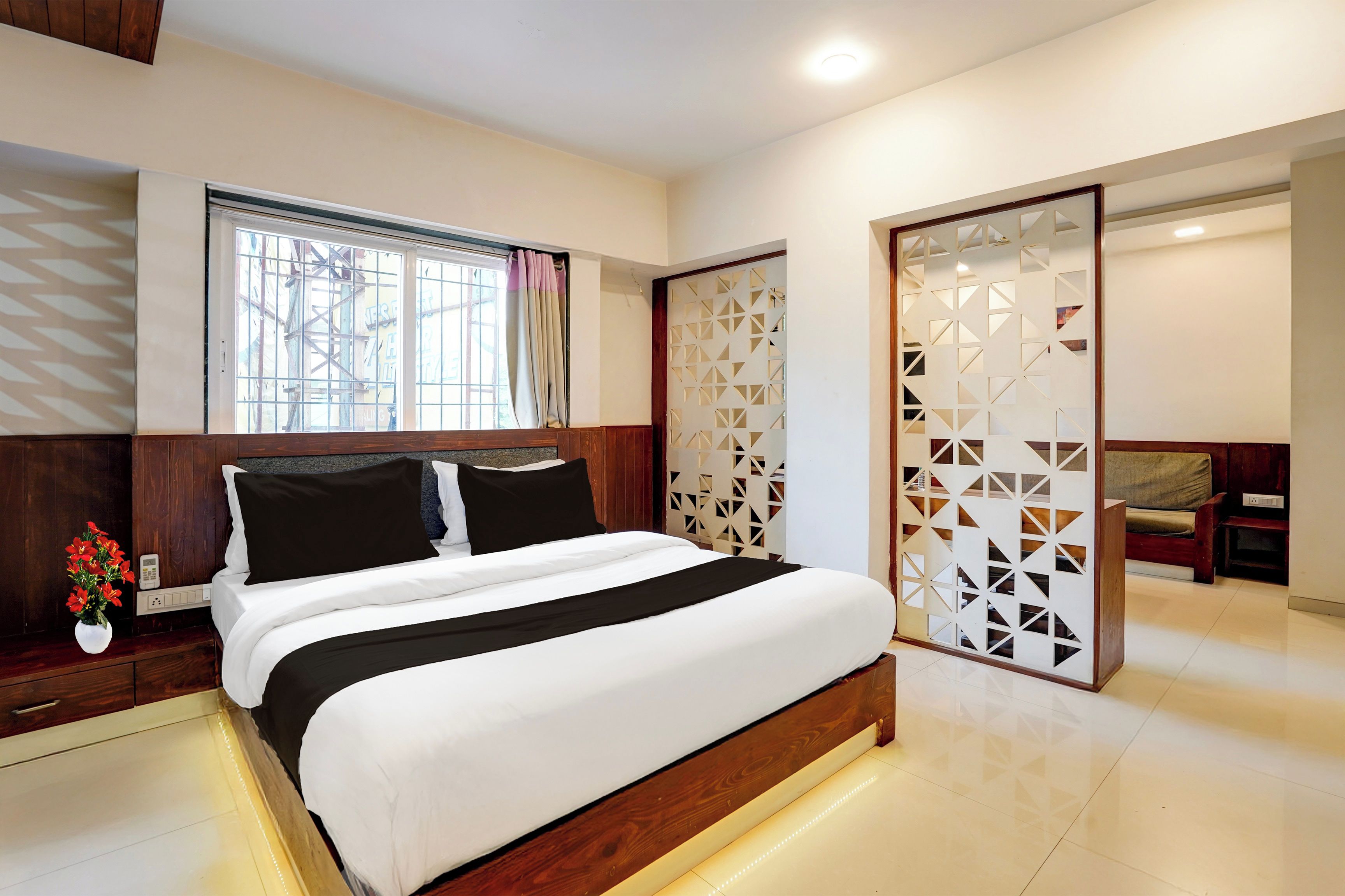 A modern bedroom with a large bed, a window with curtains, a wooden headboard, and a sliding door with geometric patterns.
