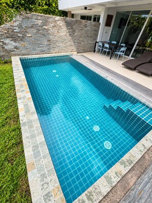 A rectangular swimming pool with a tiled edge, surrounded by a grassy area and a stone wall. - Golf view, pool villa. 5 Bed/Bath. 7 kms to Patong. Peaceful & private (Tambon Kathu)