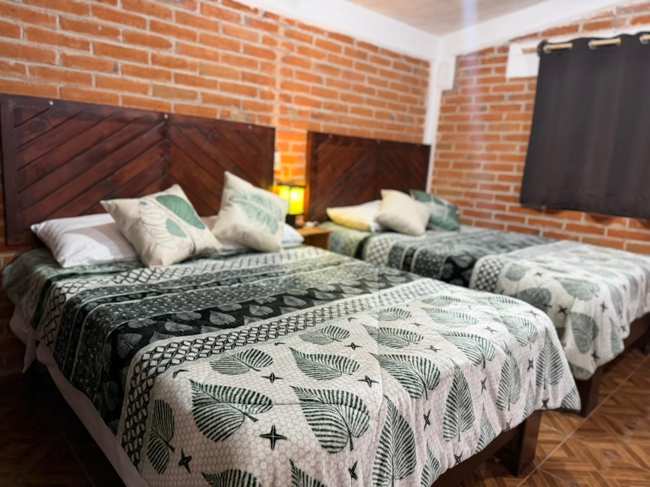 A room with two beds, each with patterned bedding and a brick wall.