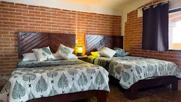 Una habitación con dos camas frente a una pared de ladrillo, cada una con cabecero de madera y ropa de cama estampada.
