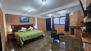 Una habitación de hotel con pared de ladrillo, una cama con ropa de cama verde, una pequeña mesa con una planta y una chimenea.