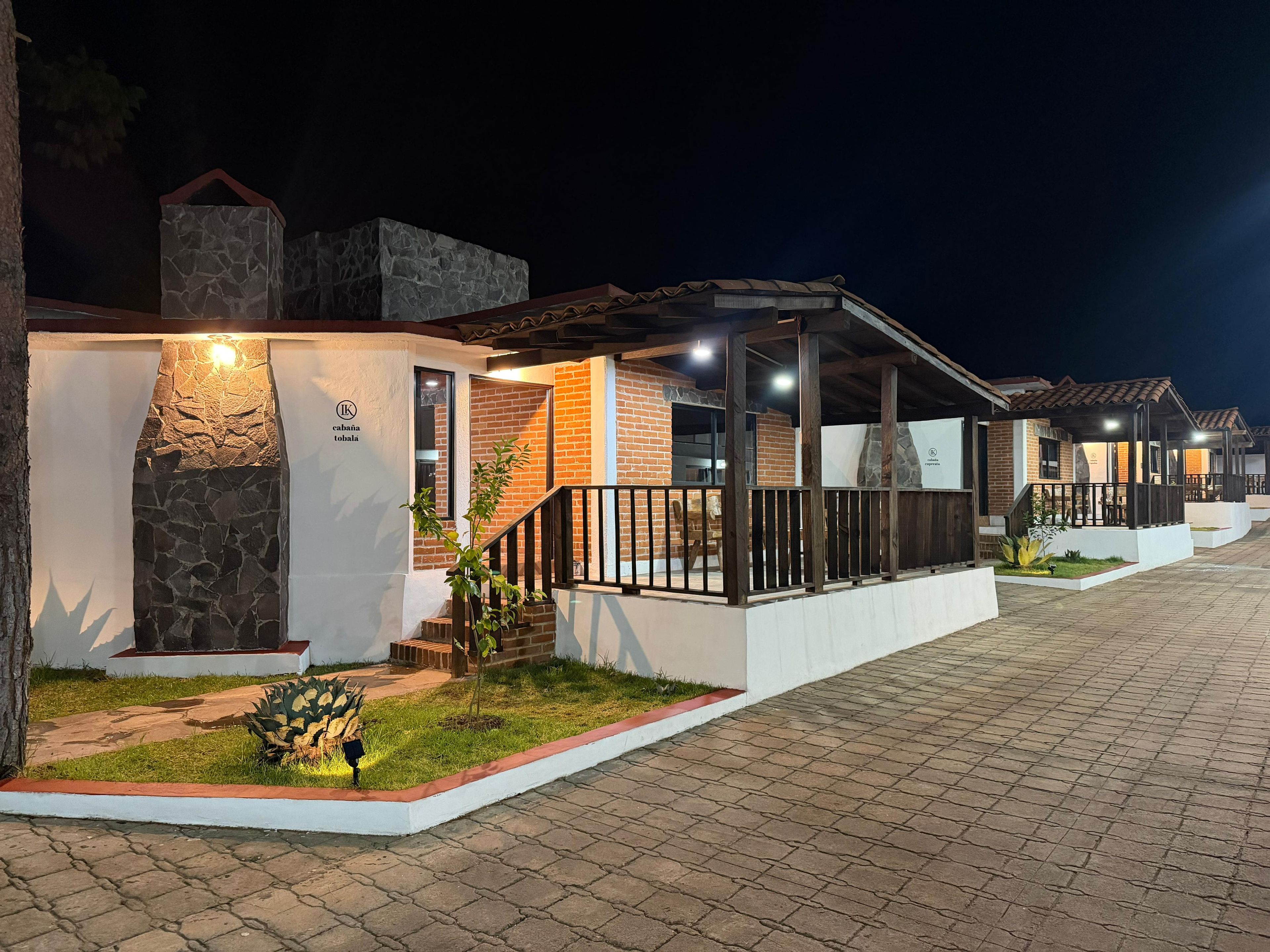 A row of hotel buildings with stone facades, outdoor seating areas, and a paved walkway.