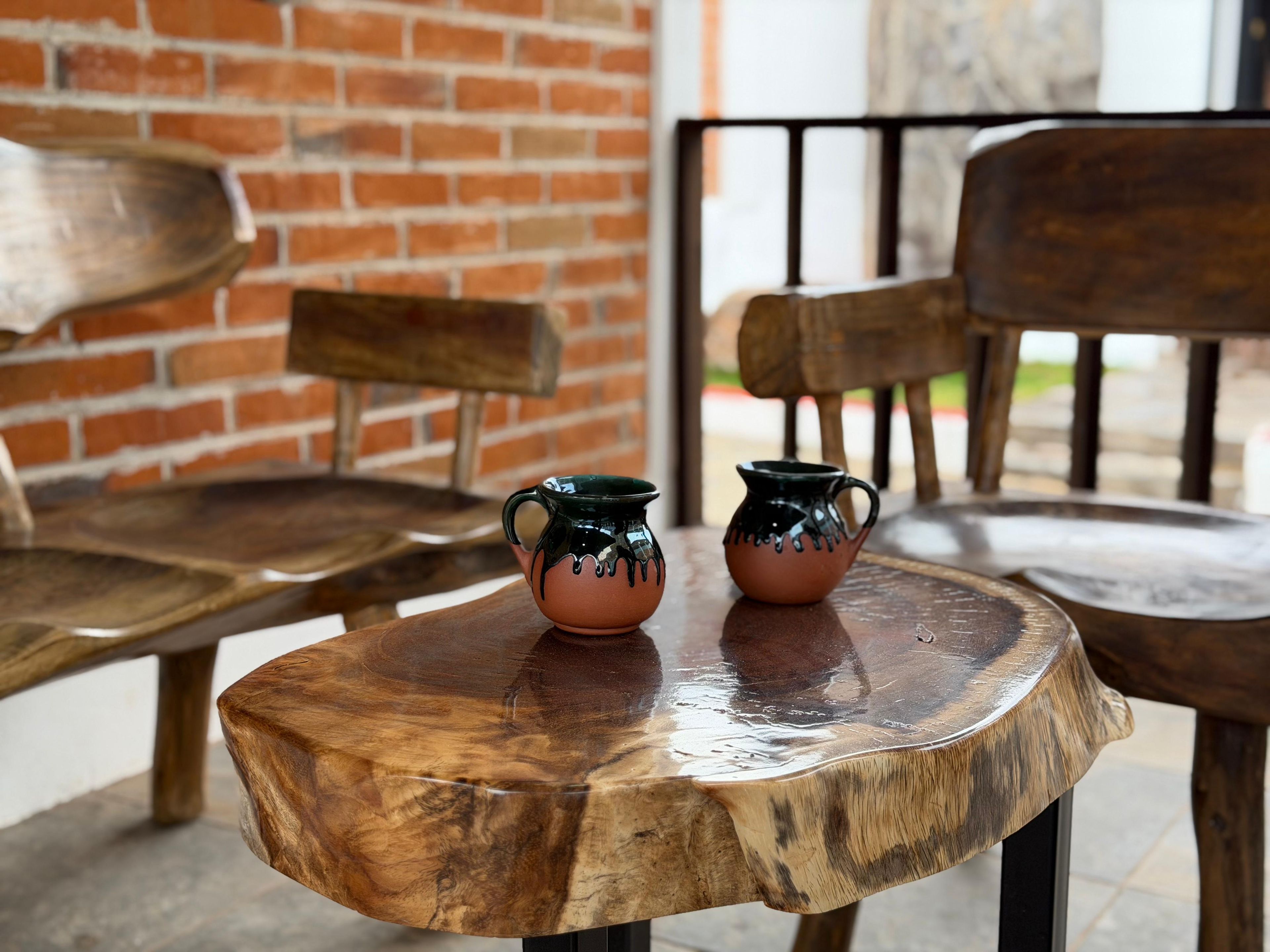 A rustic wooden table with two ceramic pitchers on it, set against a brick wall and wooden chairs.