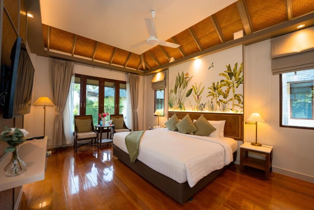 Habitación de hotel con una cama grande, un ventilador de techo, un escritorio con una silla y vistas a zonas verdes.