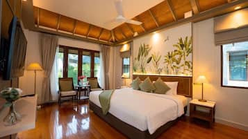 Habitación de hotel con una cama grande, un ventilador de techo, un escritorio con una silla y vistas a zonas verdes.