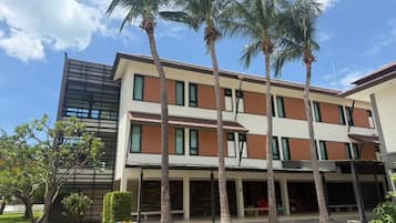 A modern building with multiple floors, a flat roof, and a covered outdoor area with palm trees.