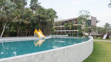 Una piscina con tobogán, rodeada de palmeras y un edificio de varios pisos.