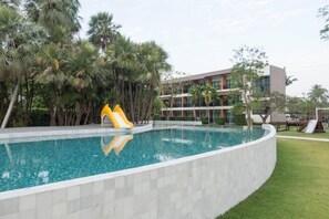 Una piscina con tobogán, rodeada de palmeras y un edificio de varios pisos.