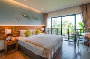 Habitación de hotel con una cama grande, una mesita de noche con un teléfono, un balcón con mesa y sillas, y vistas a zonas verdes.
