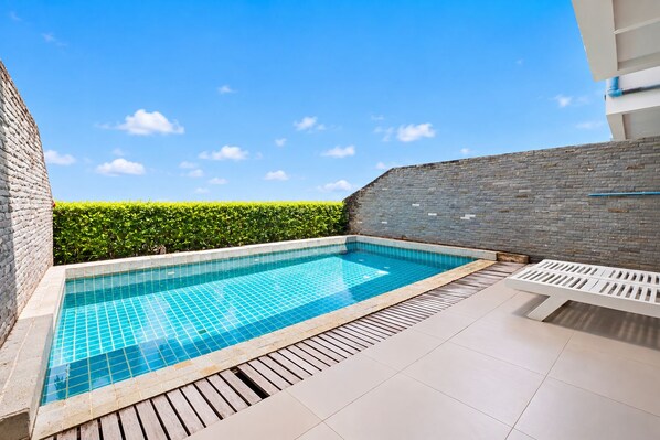 Ein rechteckiger Swimmingpool mit einer gefliesten Kante, umgeben von einem Holzboden und einer niedrigen Mauer aus Ziegeln.