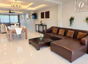 A modern living room with a brown leather sofa, a wooden coffee table, and a dining area with a wooden table and chairs. - 5 bedroom & bathroom, Golf view villa, near Patong. Peacful & private. (Tambon Kathu)