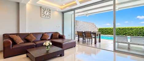 A modern living room with a leather sofa, a coffee table with flowers, and a view of an outdoor pool area.