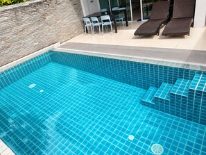 A swimming pool with a tiled edge, a stone wall, and a seating area with chairs and lounge chairs. - 5 bedroom & bathroom, Golf view villa, near Patong. Peacful & private. (Tambon Kathu)