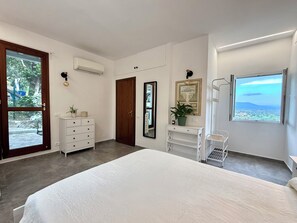 A bedroom with a large bed, a wardrobe, a desk with a plant, a mirror, and a window with a view. - Belvedere Fontepatri, a Breathtaking View of Florence (Lastra a Signa)