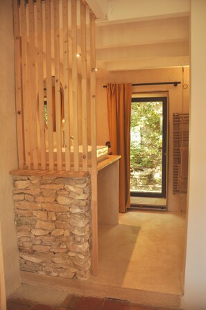 Ein Zimmer mit Steinwand, Holzlatten, einem Vorhangfenster und Blick auf Grün.