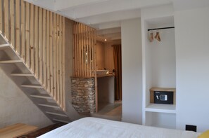 Ein Schlafzimmer mit Holzboden, einer Steinsäule, einem Bett, einem kleinen Badezimmer und einem Safe auf einem Regal.