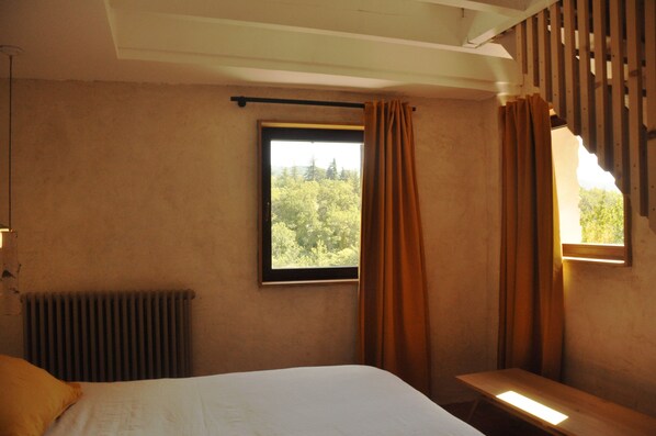 Ein Schlafzimmer mit einem Bett, einem Fenster mit Vorhängen, einem Heizkörper und einer hölzernen Bank.