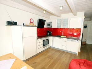 A compact kitchen with white cabinets, a microwave, a red backsplash, and a wooden floor. - Seestern at Susanne-fischer Weg 25 (Wyk auf Foehr)