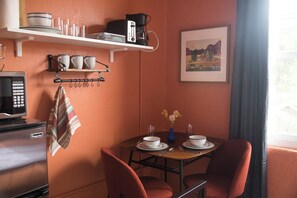 Un área de comedor compacta con una mesa dispuesta para dos personas, un microondas, una tetera y una cafetera en la pared.