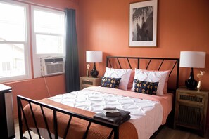 A hotel room with a bed, two bedside tables with lamps, a window with curtains, and a wall-mounted picture.