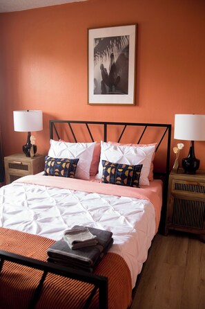 A neatly made bed with a white and pink duvet, two pillows with a geometric pattern, and a folded towel on the bed.