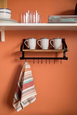 A kitchen shelf with white cups and a striped cloth hanging below.