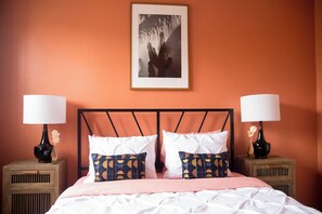 Una habitación de hotel con una cama, dos mesitas de noche con lámparas y un cuadro en la pared.