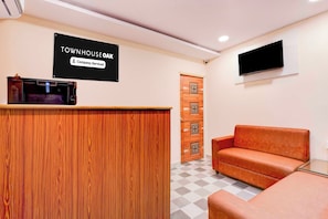 A reception area with a wooden reception desk, a sign indicating 'TOWNHOUSE' and 'Company-Serviced,' a television mounted on the wall, and a checkered floor. - Townhouse Oak Visakhapatnam Lumbini Park (Visakhapatnam)