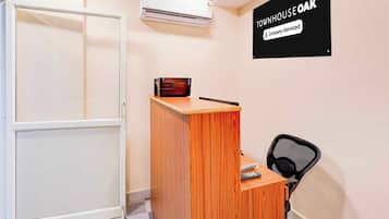 A room with a wooden desk, a black office chair, a white air conditioning unit, and a wall-mounted sign.