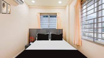 A bedroom with a bed, a window with blinds, a nightstand, and a vase with flowers.