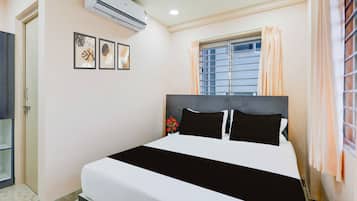 A bedroom with a bed, an air conditioner, a window with curtains, and wall art.
