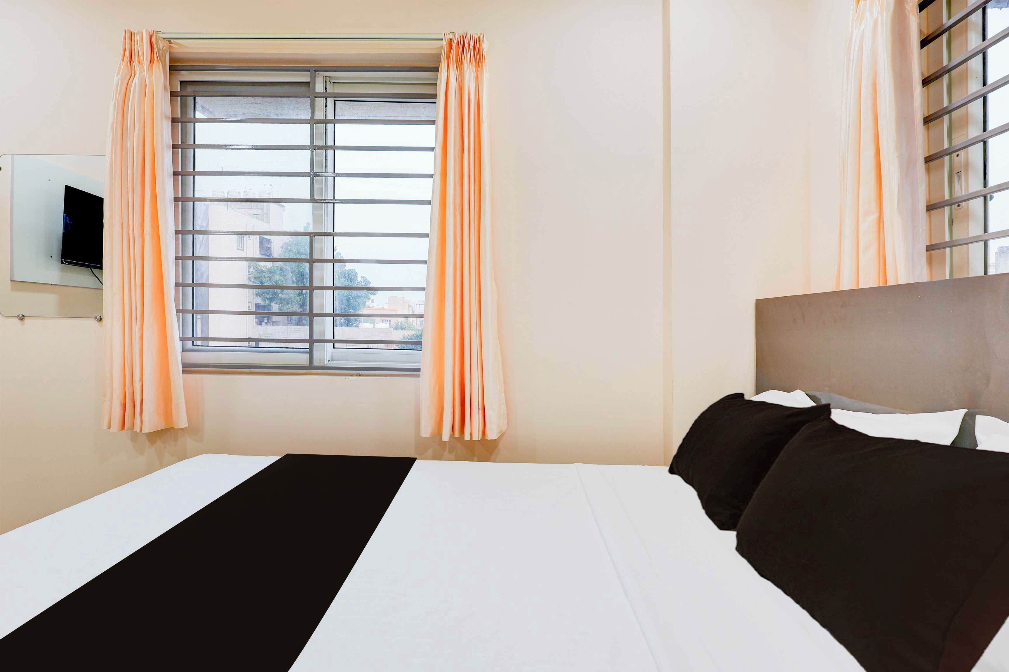 A hotel room with a bed, a television on the wall, and a window with curtains.