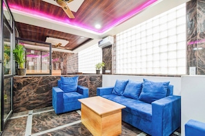 Un interior moderno con un sofá azul, una mesa de centro de madera y un techo con listones de madera e iluminación rosada.
