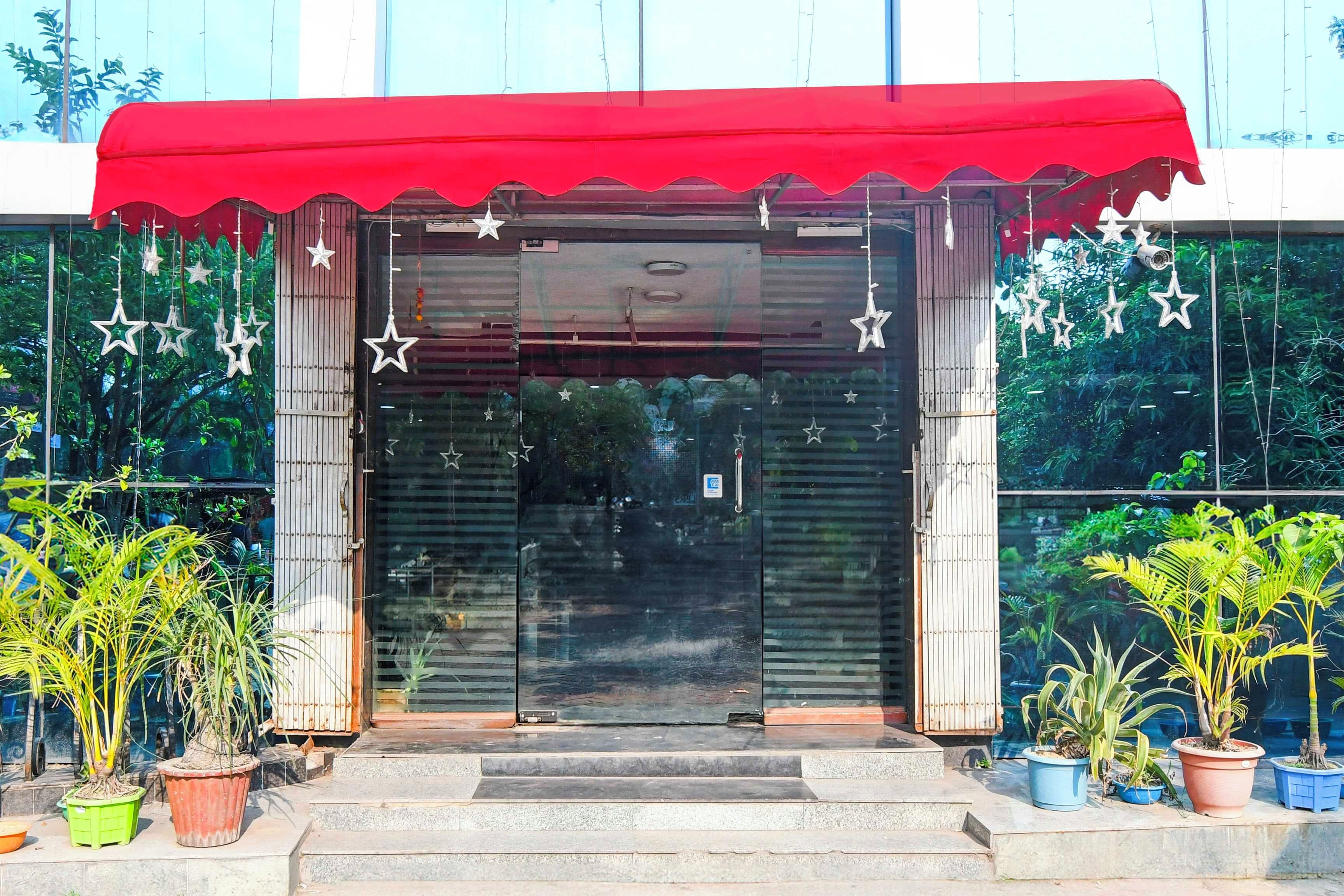 Entrada de um edifício com toldo vermelho, portas de vidro e decorações em formato de estrela.