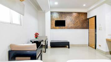 Habitación de hotel con dos camas, una mesita con un florero, una banca, un televisor instalado en una pared con textura y una puerta de madera.