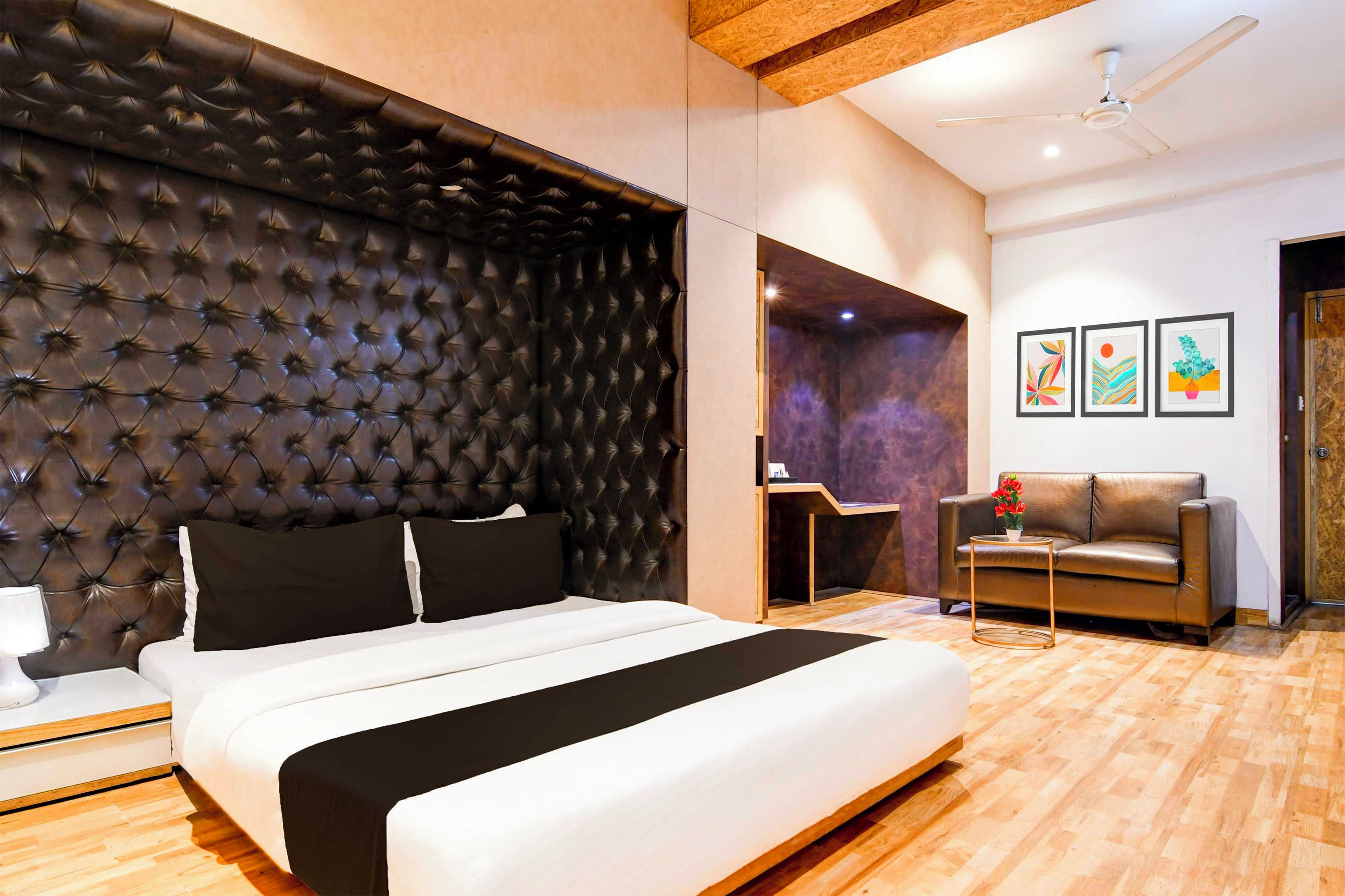 A modern bedroom with a tufted headboard, a bed with white bedding, a brown leather sofa, a small round table, and a ceiling fan.