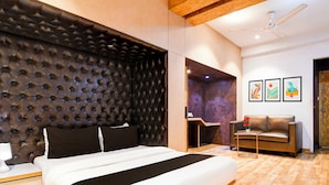 Un dormitorio moderno con un cabecero acolchado, una cama con ropa de cama blanca, un sofá de cuero marrón, una pequeña mesa redonda y un ventilador de techo.