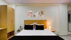Hotellihuone, jossa on sänky, yöpöydät, puinen vaatekaappi ja kolme kehystettyä taideteosta seinällä.