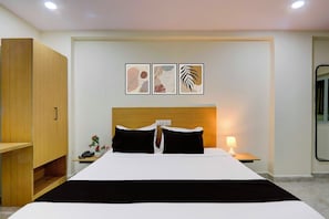Una habitación de hotel con una cama, mesitas de noche, un armario de madera y tres cuadros enmarcados.
