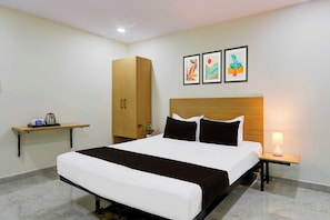 Una habitación de hotel con cama, mesita de noche, estante con artículos de aseo, armario y tres cuadros en la pared.