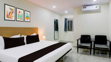 Une chambre d’hôtel comprenant un lit, un bureau, deux chaises, un miroir et trois œuvres d’art encadrées accrochées au mur.