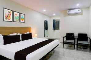 Habitación de hotel con cama, escritorio, dos sillas, un espejo y tres cuadros en la pared.