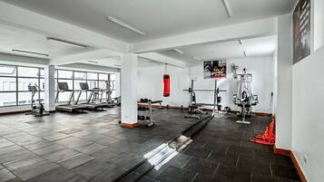 Uma academia com equipamentos de ginástica, janelas amplas e um saco de pancadas vermelho.
