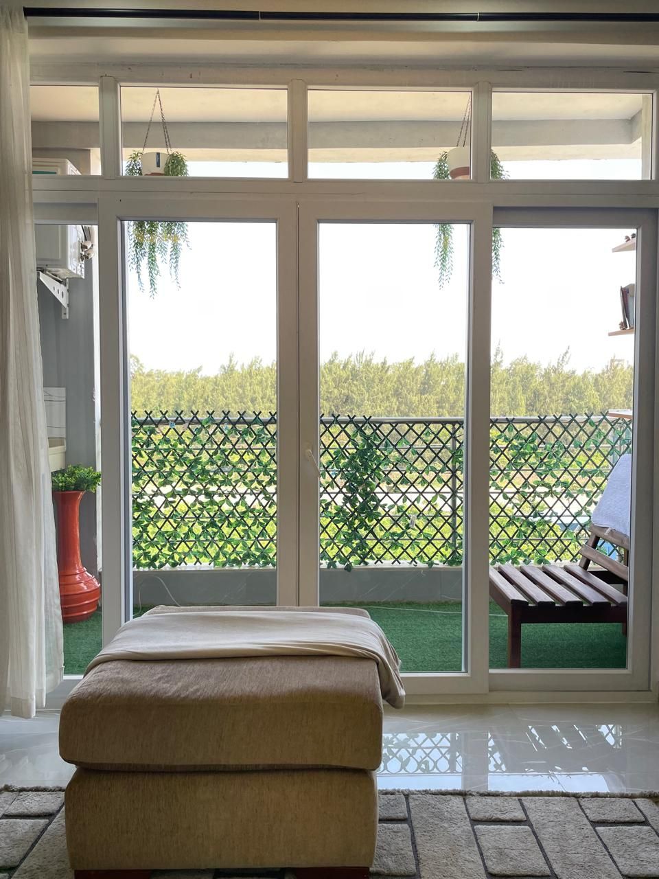 Ein Zimmer mit einer großen Schiebeglastür, die auf einen Balkon mit Blick auf einen grünen Zaun und Bäume führt.