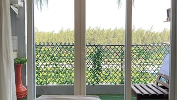 Ein Zimmer mit einer großen Schiebeglastür, die auf einen Balkon mit Blick auf einen grünen Zaun und Bäume führt.